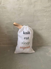 Project bag with embroidered text "knit, eat, sleep, repeat", standing