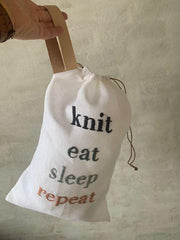 Project bag with embroidered text "knit, eat, sleep, repeat", hanging